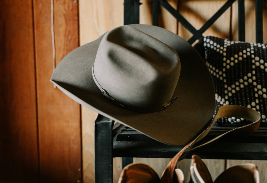 Gray cowboy hat displayed on a black metal shelf against a wooden background, showcasing its unique design and craftsmanship.
