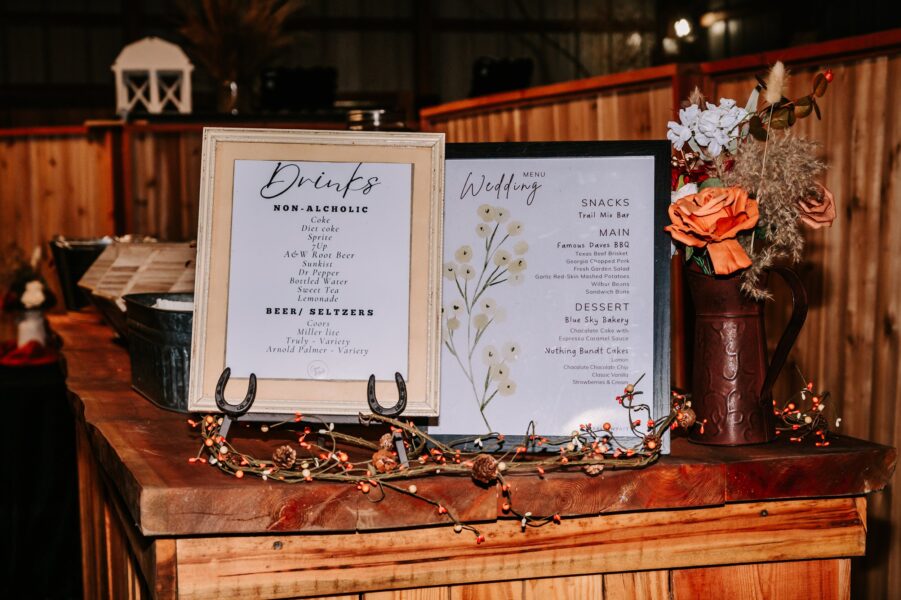 Wedding reception drink and menu display featuring a non-alcoholic drink list, beer options, and a detailed menu with snacks, main courses, and desserts. The setup includes decorative flowers and rustic wooden elements, creating a warm atmosphere.