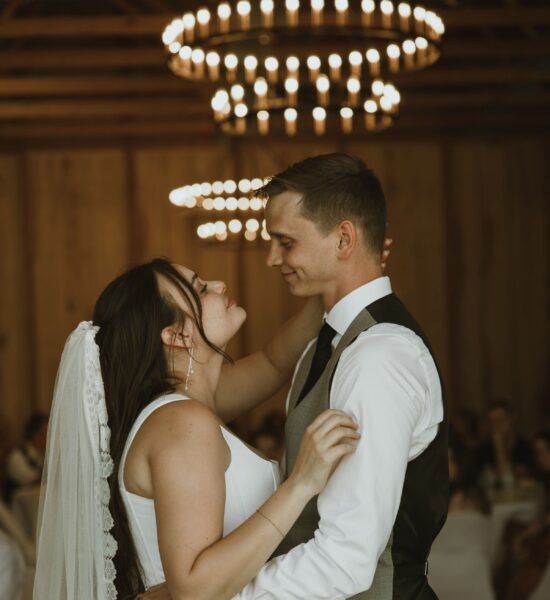 Bride and groom sharing an intimate moment during their first dance at a wedding reception, surrounded by elegant chandeliers and a warm wooden backdrop.