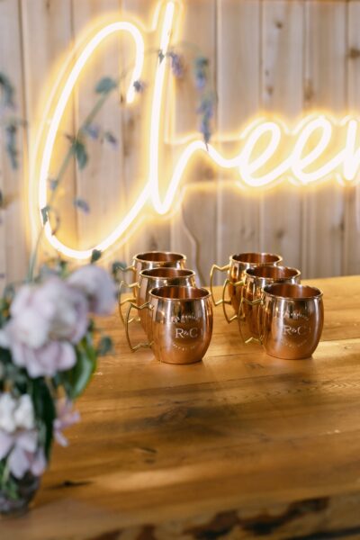 Copper mugs arranged on a wooden table with a neon 